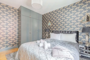 A bedroom with a bed, a wardrobe, a nightstand, and a patterned wall.