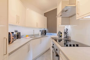 A modern kitchen with white cabinets, a black stovetop, and a stainless steel sink.