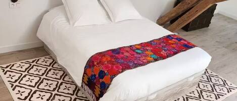 A bed with a white mattress and pillows, a colorful blanket, and a patterned rug on a wooden floor.
