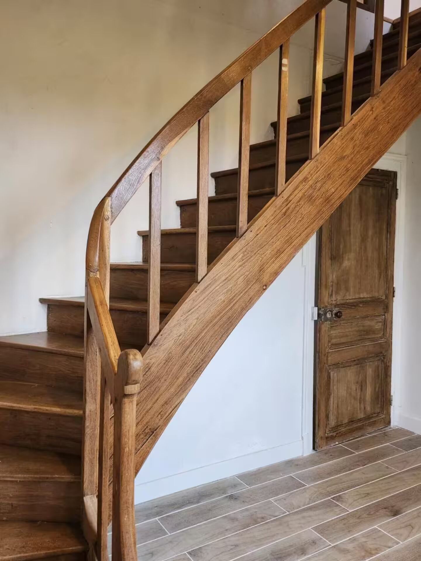 A wooden staircase with a handrail, leading to a door with a metal handle.