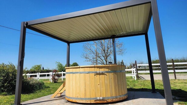 Un tonneau en bois, placé sous un abri en métal, avec un ciel bleu clair en arrière-plan.