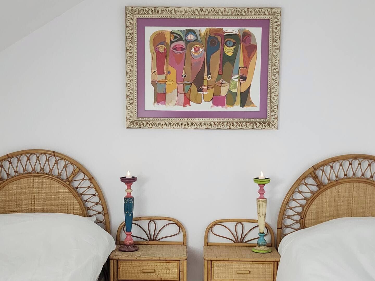 Une chambre avec deux lits, chacun doté d’une tête de lit en osier, d’une œuvre d’art accrochée au mur et de deux tables de chevet avec des bougies.