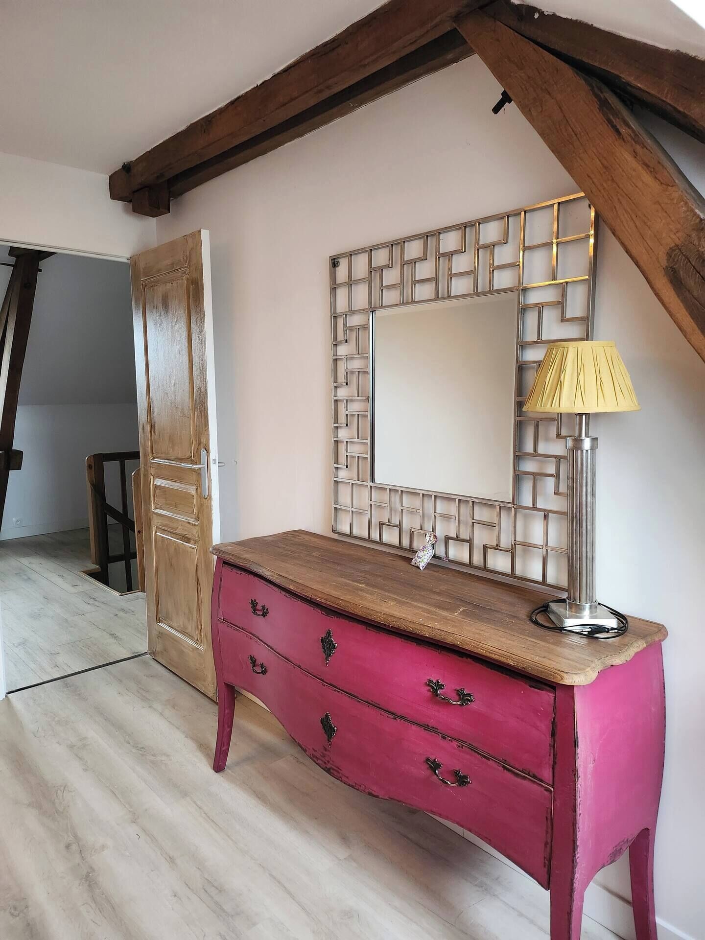 Een kamer met een houten dressoir, een spiegel met een geometrisch kader en een lamp.