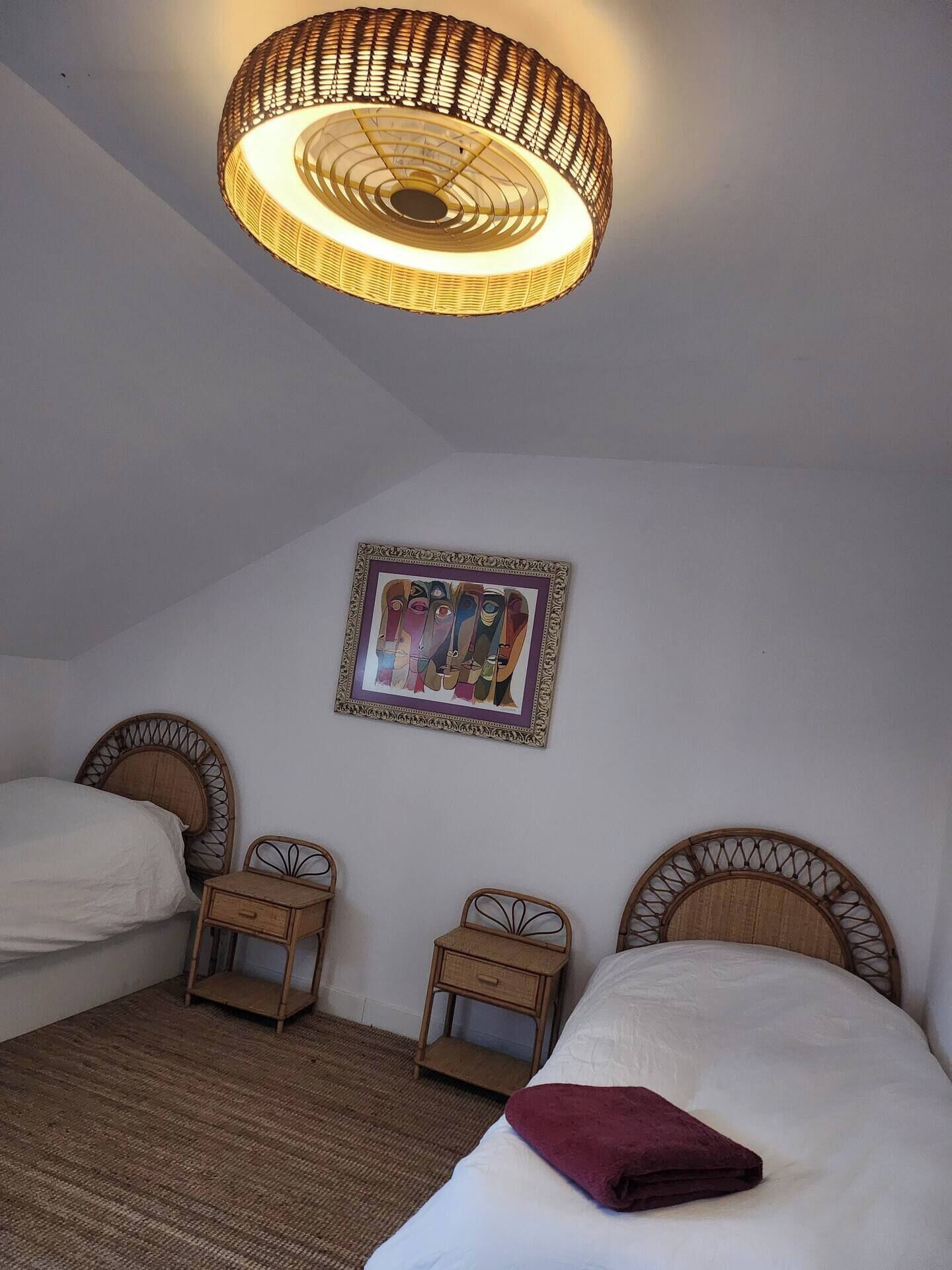A bedroom with two beds, a hanging light fixture, a framed artwork, and a small bedside table.