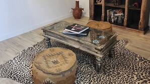A living room with a glass coffee table, a leopard print rug, a wooden cabinet with books, and a framed painting. - Lady Rose room (Maisonnais)