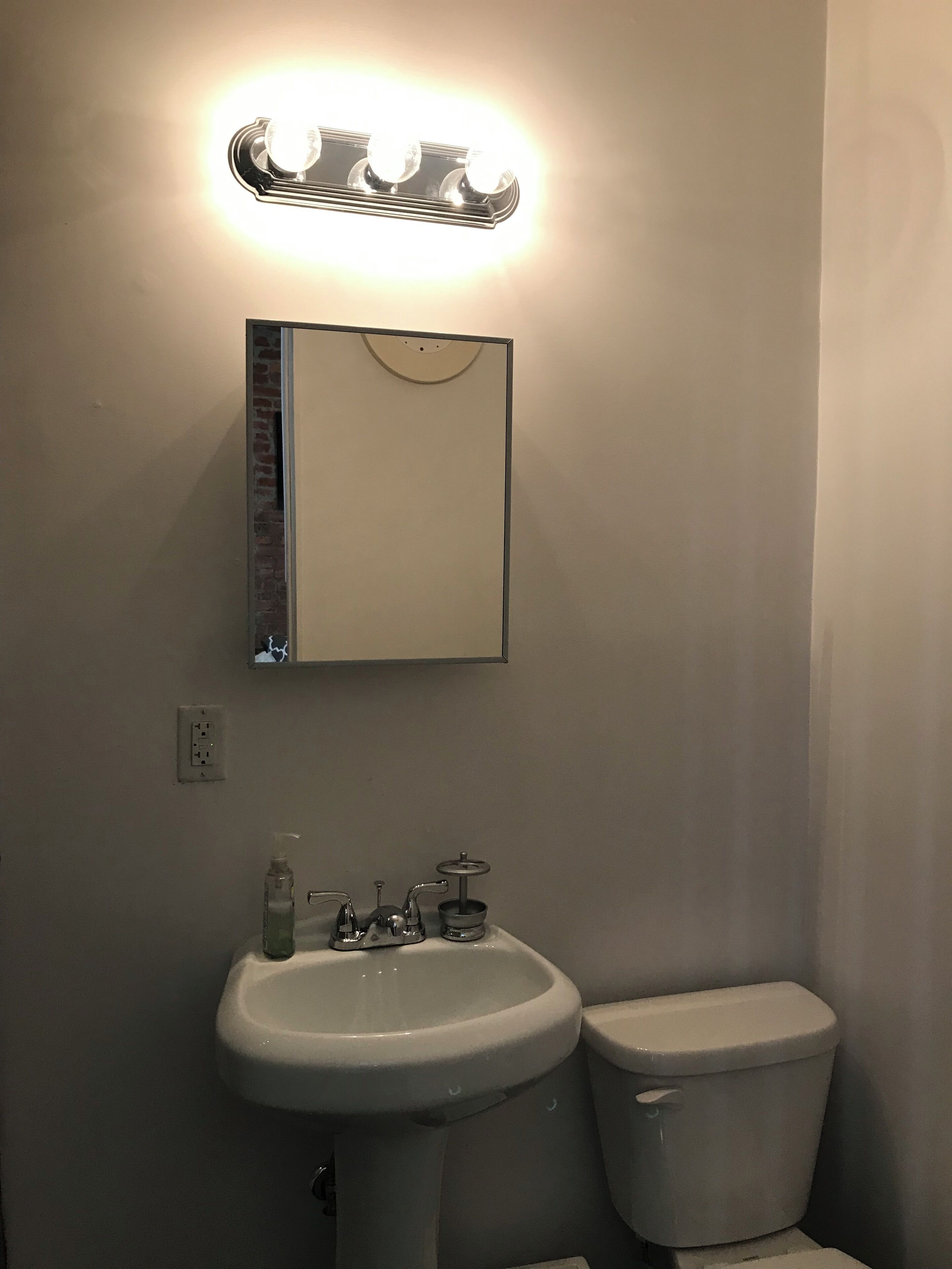 Une salle de bain avec un lavabo blanc, des toilettes et un miroir au-dessus du lavabo.