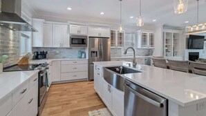 Une cuisine moderne avec des meubles blancs, des appareils en acier inoxydable et des luminaires suspendus.