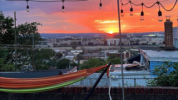 A rooftop terrace with a view of the sunset over a cityscape, featuring a hammock and string lights. - Charming apartment near Manhattan. Perfect for a getaway in NYC (North Bergen)