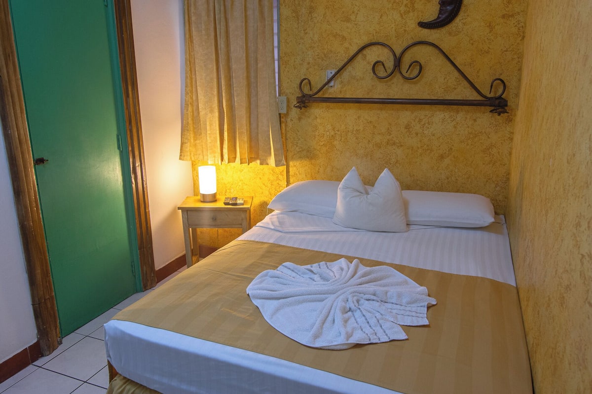 Habitación de hotel con cama, mesita de noche con lámpara y un adorno en la pared.