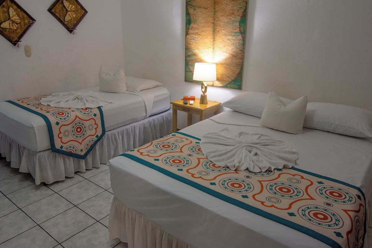 Habitación de hotel con dos camas, una mesita de noche, una lámpara y decoración en la pared.