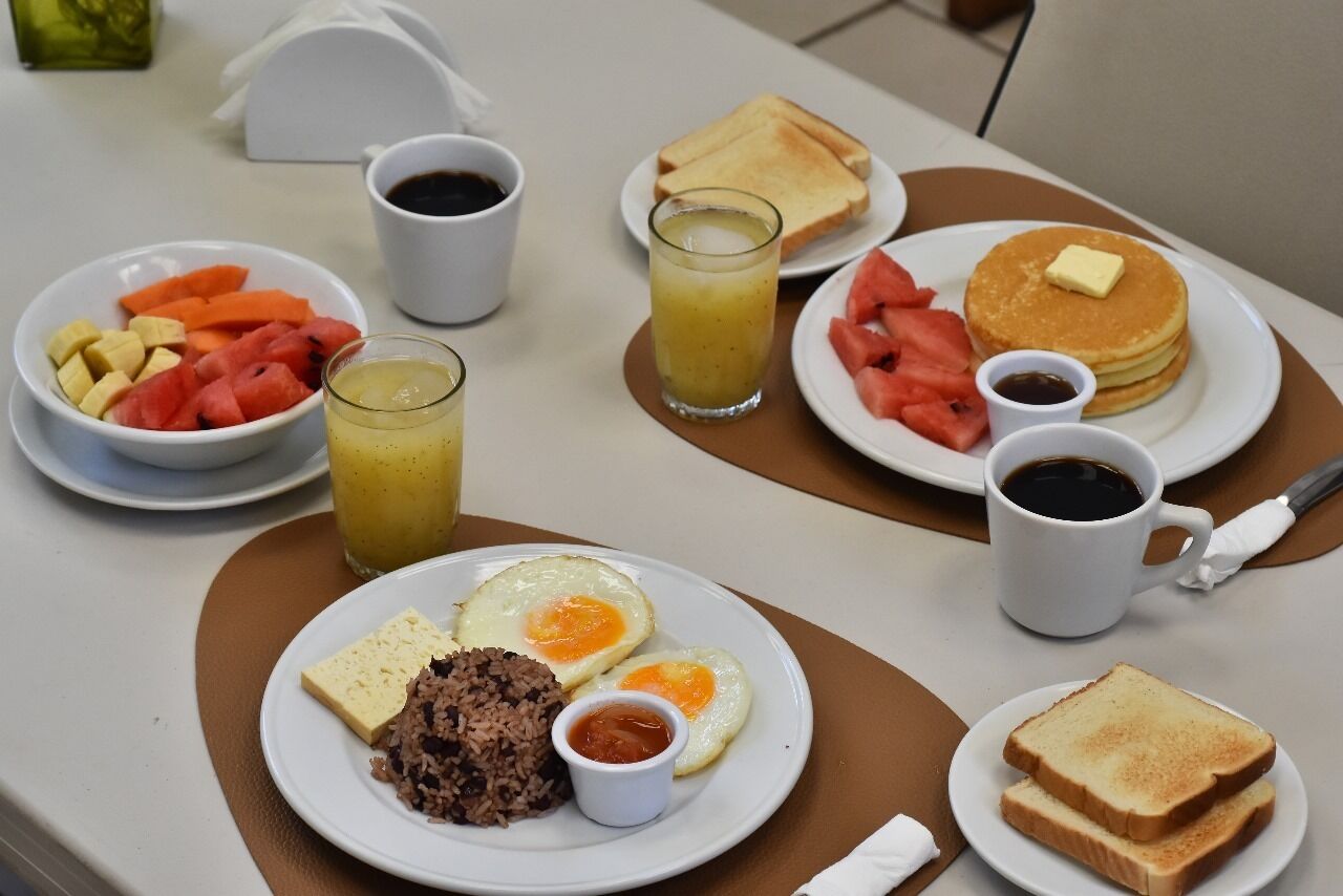 A breakfast setting with plates of eggs, toast, pancakes, and fruit.