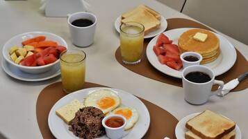 A breakfast setting with plates of eggs, toast, pancakes, and fruit.