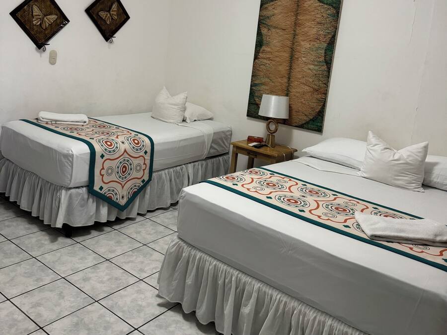 A hotel room with two single beds, a large painting on the wall, and a small table with a lamp.