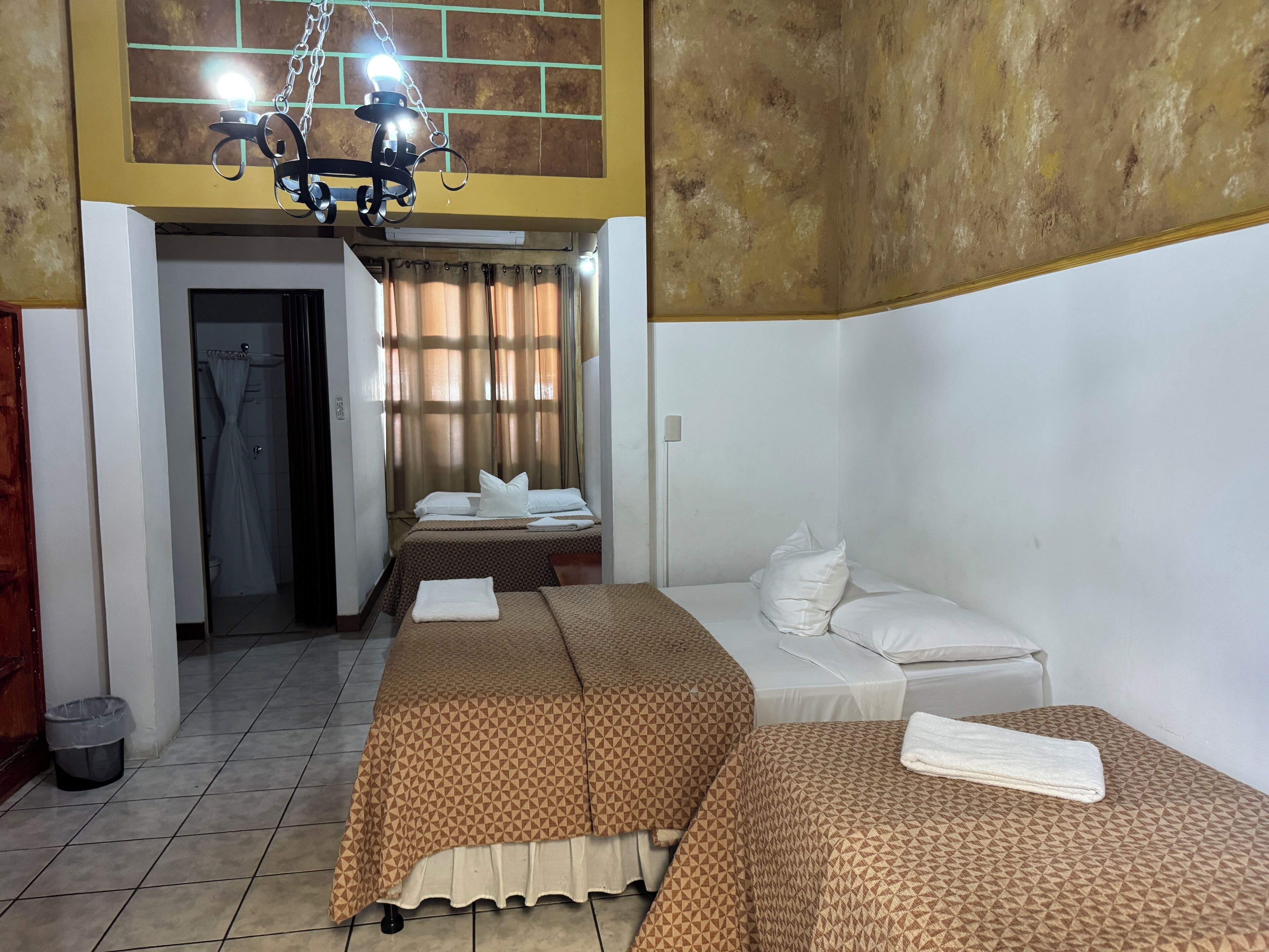 Une chambre d’hôtel avec deux lits, un espace douche et un lustre.