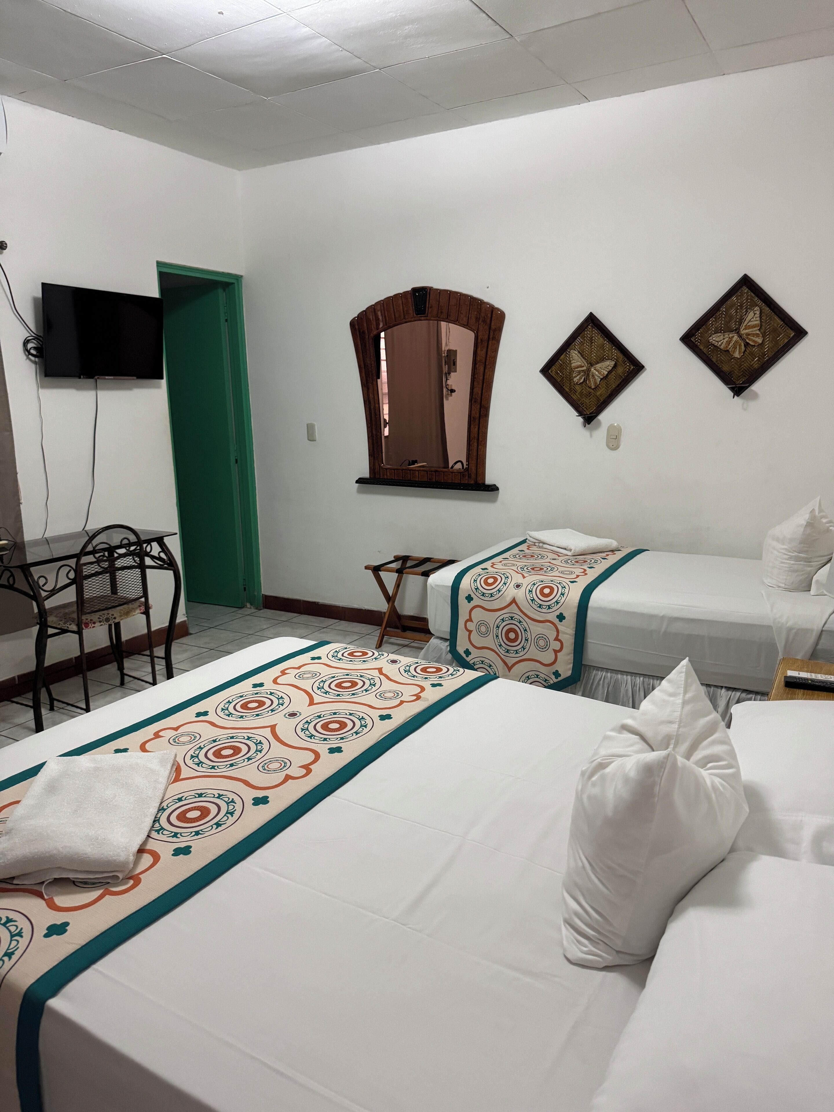 Une chambre d’hôtel avec deux lits, un bureau, une chaise, une télévision et un miroir.