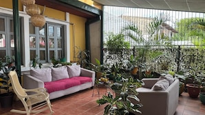 A cozy patio area with a white sofa, a rocking chair, and various potted plants. - La Posadita de Bolonia (Managua)