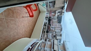 A balcony with a view of a densely packed urban area, a tiled floor, and a red chair. - Apartment with two bedrooms, one with a double bed and one with two beds (Saranda)