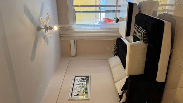 A modern living room with a sofa, a ceiling fan, and a window with curtains. - Apartment with two bedrooms, one with a double bed and one with two beds (Saranda)
