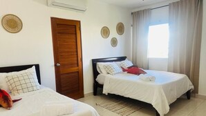 A hotel room with two beds, a wooden door, a window with curtains, and wall decorations. - Sunrise Family Hub (Punta Cana)