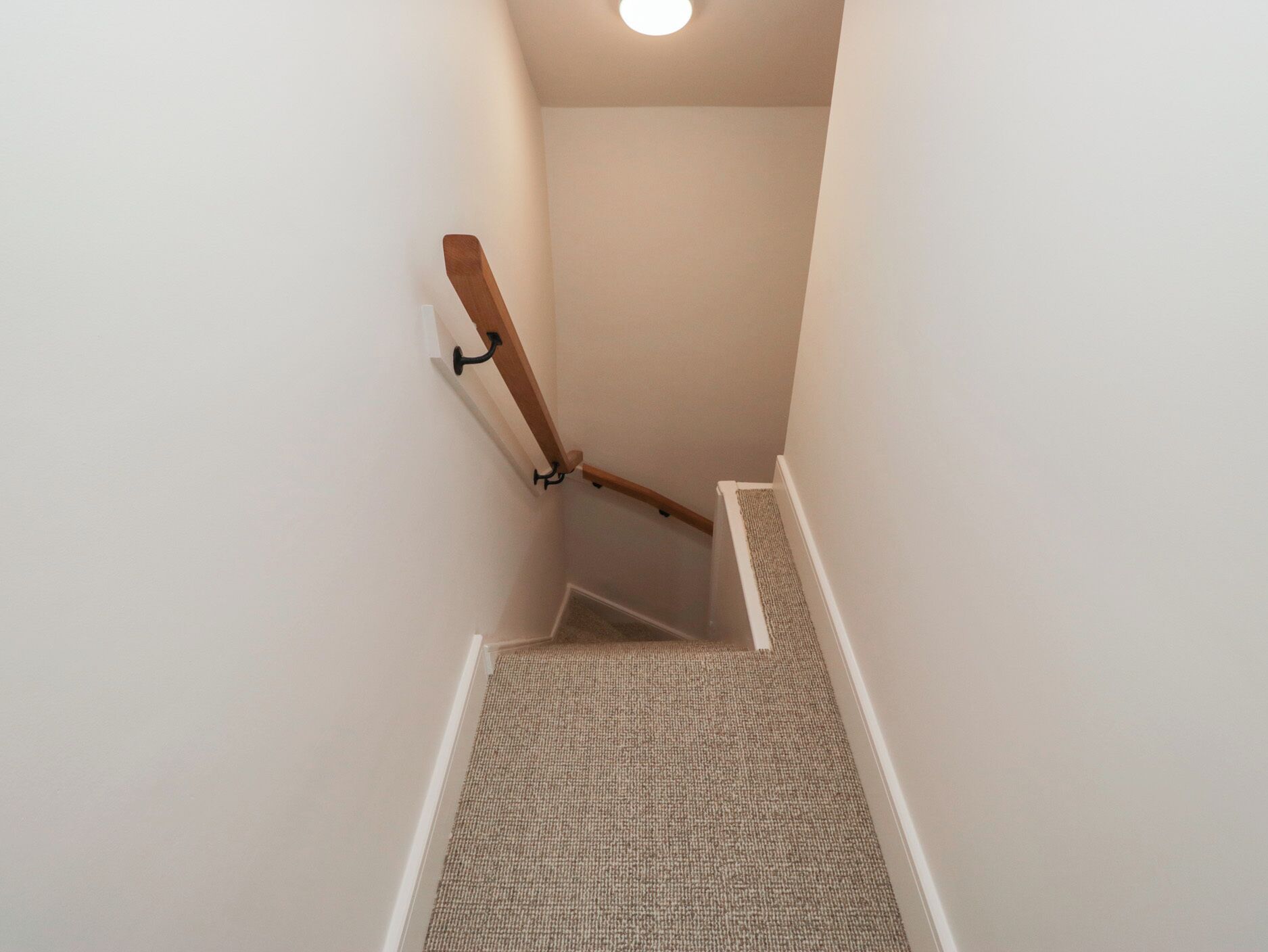 Una escalera estrecha con barandilla de madera y peldaños alfombrados.