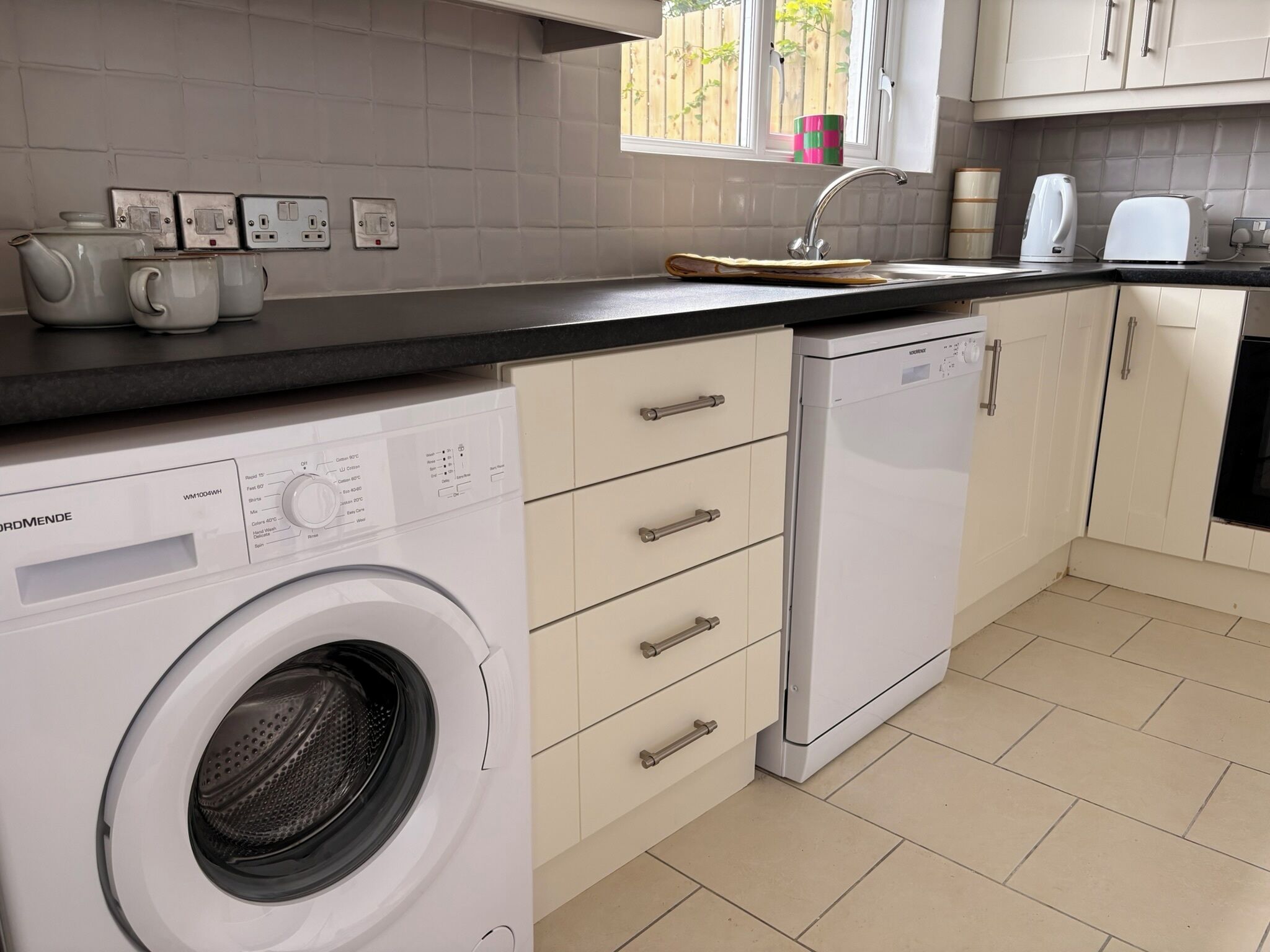 A compact kitchen with a built-in washer, a sink, and a window with a view of the outside.