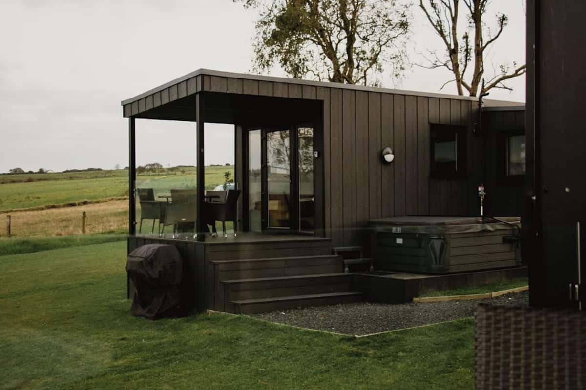 Eine moderne Außenanlage mit überdachter Sitzgelegenheit, Whirlpool und Blick auf die umliegende Landschaft.