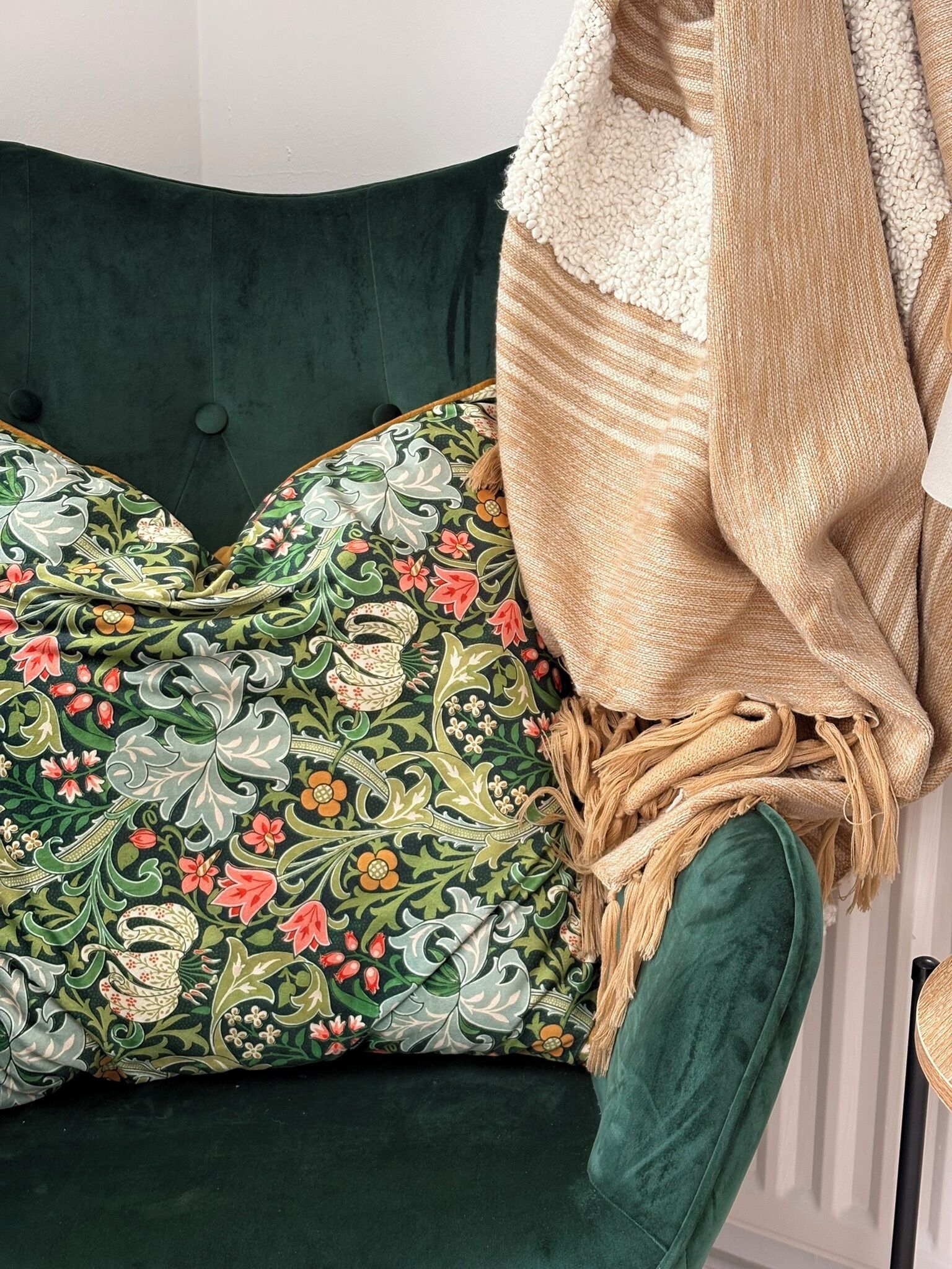 Un sofá verde con cojines estampados y una manta color beige.