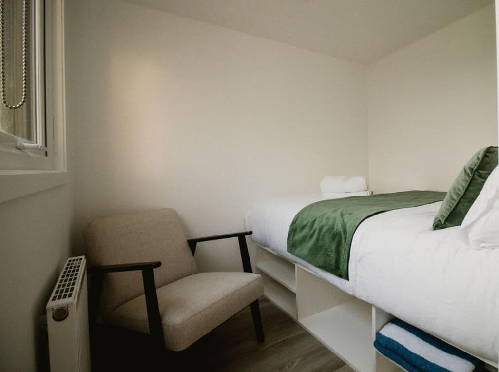 A small, neatly arranged bedroom with a single bed, a chair, and a radiator.