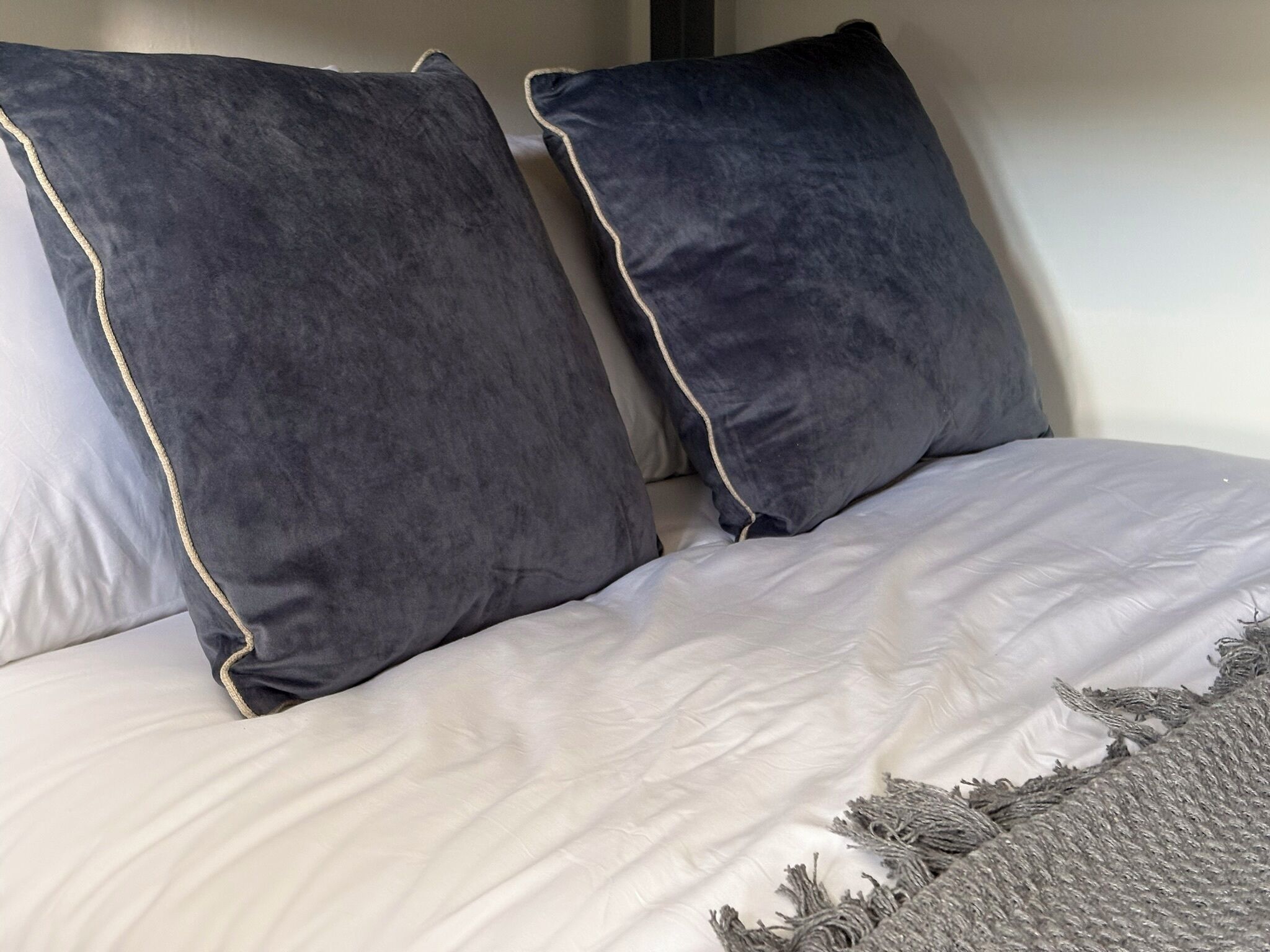 A bed with white bedding and two dark pillows with a light trim.