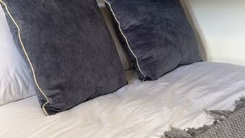 A bed with white bedding and two dark pillows with a light trim.