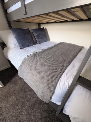 Un lit superposé avec une couverture tricotée grise, des oreillers blancs et une tête de lit en bois.