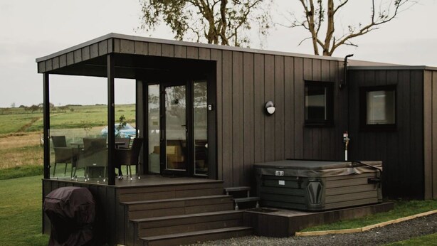 A modern outdoor structure with a glass-enclosed patio, a hot tub, and a covered seating area. - Aganmore Farm Glamping (Ballycastle)