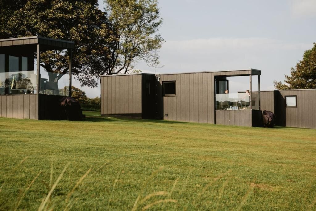 A modern building with a glass enclosure, a wooden deck, and a grassy area.