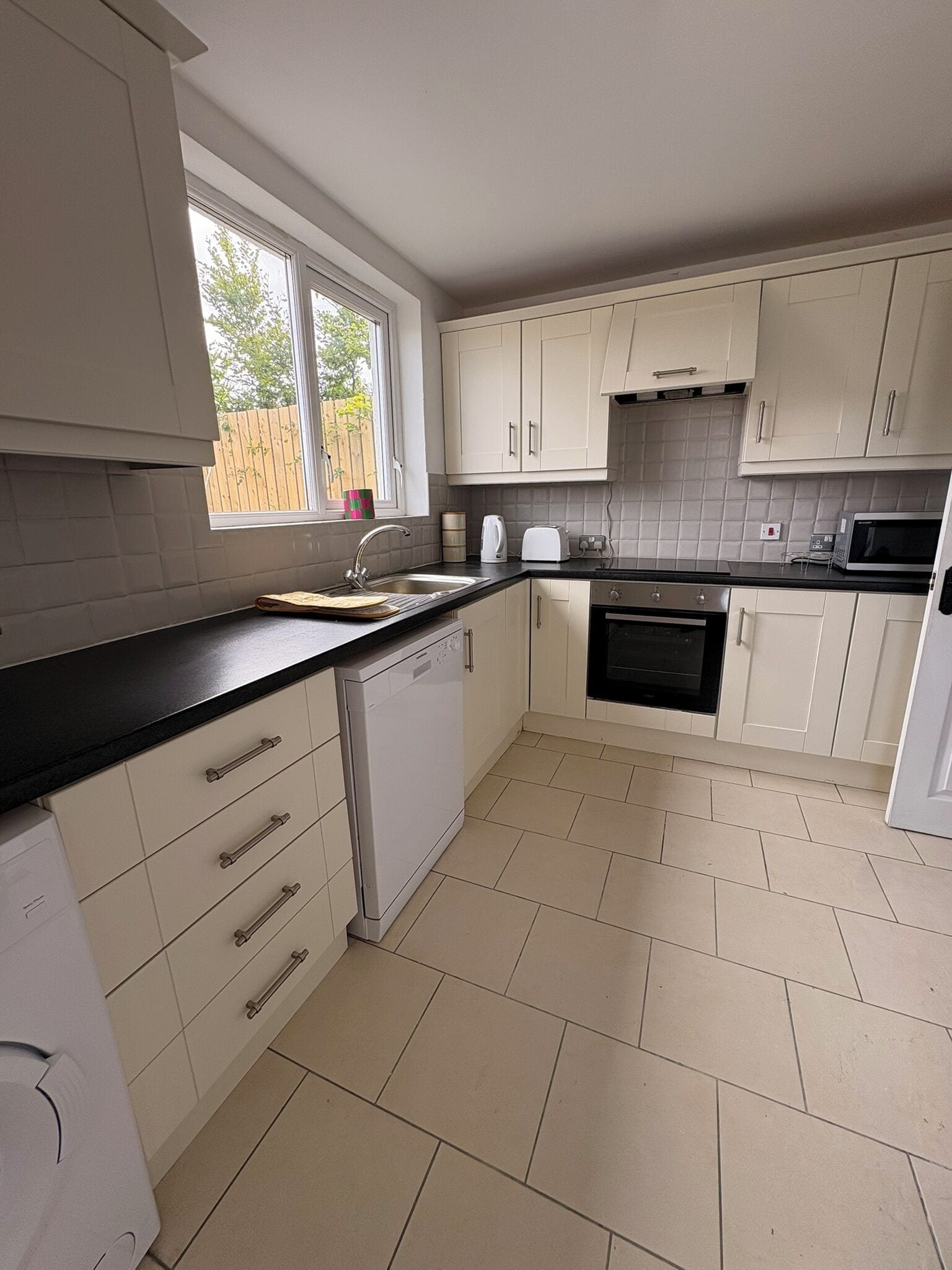 A kitchen with white cabinets, a black countertop, a dishwasher, an oven, and a microwave.