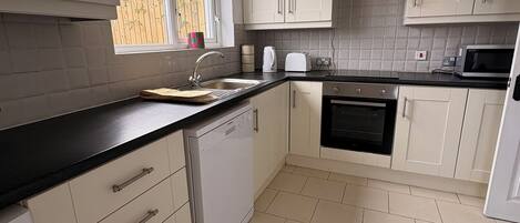 A kitchen with white cabinets, a black countertop, a dishwasher, an oven, and a microwave.
