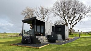 A modern, compact outdoor structure with a glass enclosure, a hot tub, and a small seating area. - Aganmore Farm Glamping (Ballycastle)