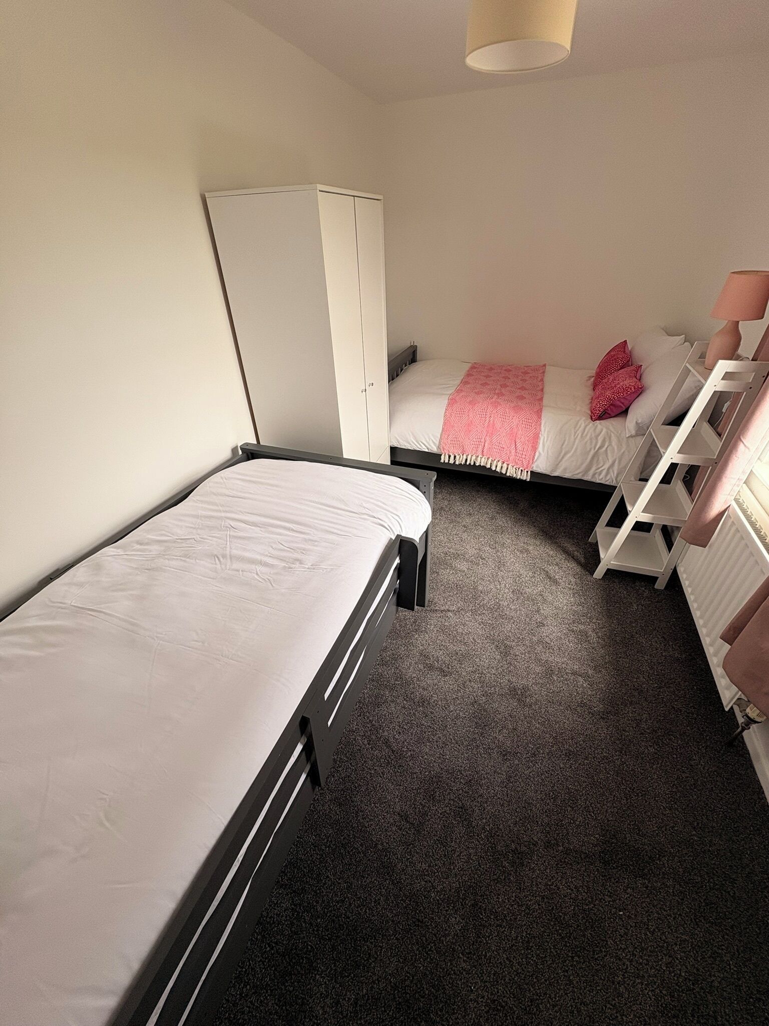 A bedroom with two single beds, a wardrobe, a radiator, and a shelf unit.