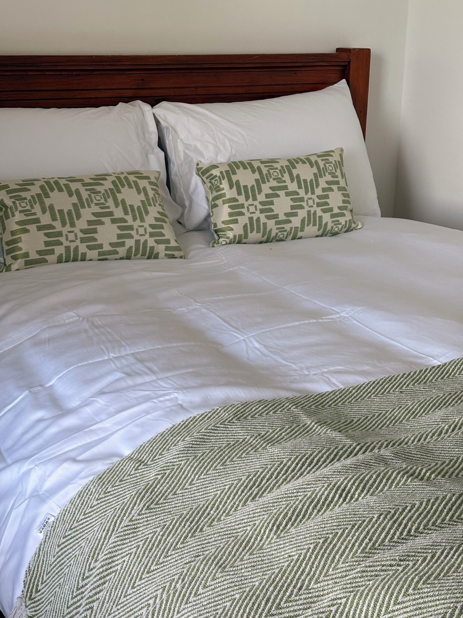 A neatly made bed with white linens and two pillows with a green leaf pattern.