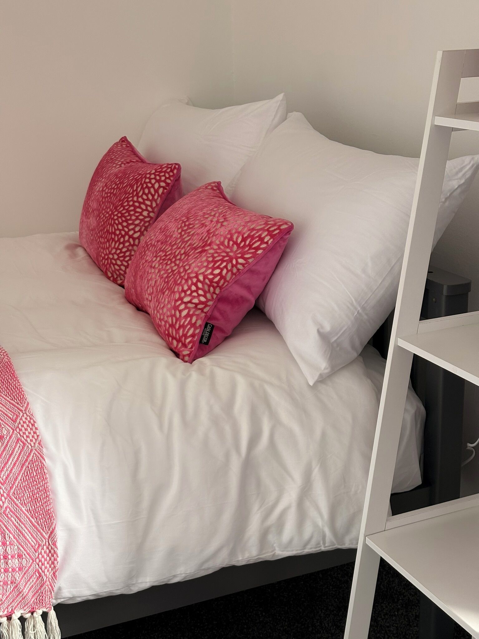 A bed with white bedding and two pink pillows.
