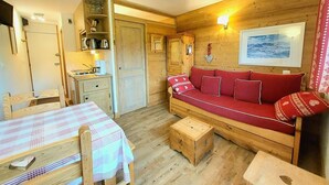 L’intérieur chaleureux d’un chalet avec une table à manger en bois, un canapé rouge et un petit coin cuisine.