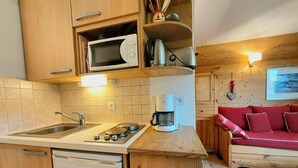 Une cuisine compacte équipée d’un évier, d’une cuisinière et d’un four à micro-ondes. On y trouve un canapé rouge et une petite table avec une machine à café.