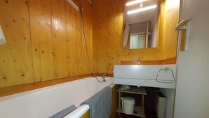 Une petite salle de bain aux dimensions réduites, avec des murs en bois, un lavabo blanc et une baignoire.