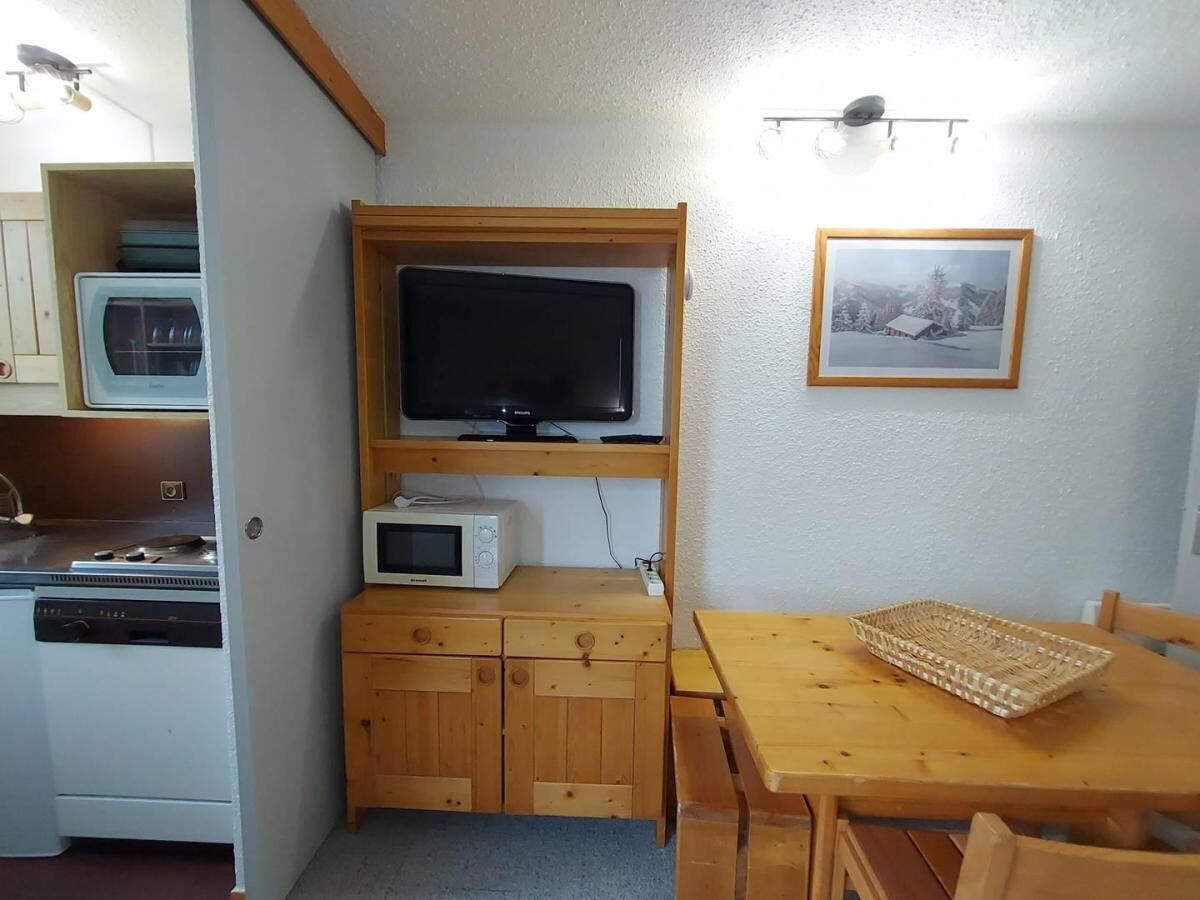 Une cuisine compacte équipée d’un four à micro-ondes, d’un petit réfrigérateur et d’un meuble en bois. On y trouve une table en bois, un panier tressé et un tableau encadré accroché au mur.