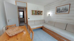 Une pièce comprenant une table à manger en bois, un canapé beige, une petite bibliothèque et un tableau encadré accroché au mur.