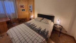 A bedroom with a bed, a nightstand, a desk, and a chair.