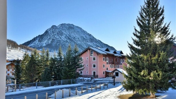 A hotel with a mountain backdrop, snow-covered ground, and a clear sky.