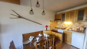 A dining area with a wooden table set for four, a kitchen with wooden cabinets and a tiled backsplash, and pendant lights above the table.