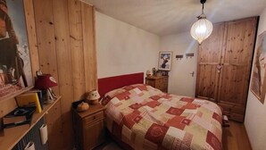 Un dormitorio con un armario de madera, una cama con colcha, una mesita de noche, una lámpara y una luz en el techo.