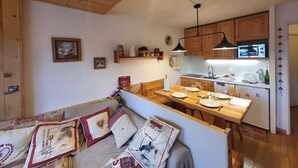 Una sala de estar acogedora con techo de madera, un comedor con mesa de madera y una cocina con armarios de madera y microondas.