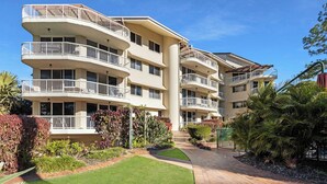 A multi-story residential building with balconies, a paved pathway, and landscaped gardens. - Unit 13 Charlton on the Esplanade (Torquay)